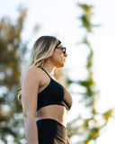Woman in black athletic wear standing outdoors with blurred natural background