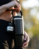 Person holding a black insulated container with a protein powder jar attached, outdoors.