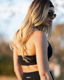 Woman wearing a black sports bra and leggings with sunglasses outdoors.