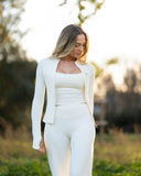 Woman in a white outfit standing in a natural setting with trees and grass.