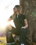Woman in black outfit sitting against a tree with a black water bottle