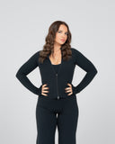 Woman wearing a black zip-up jacket and pants on a gray background