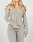 Woman wearing a gray long-sleeve top and leggings with a visible brand logo on a white background