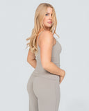 Woman wearing a beige sleeveless top and pants on a light gray background