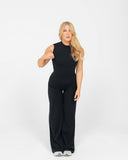 Woman wearing a black sleeveless top and wide-leg pants on a white background