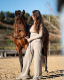 Woman in a beige outfit standing next to a brown horse in an outdoor setting