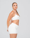 Woman wearing a white sports bra and shorts set on a gray background