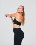 Woman wearing a black sports bra and leggings on a light gray background